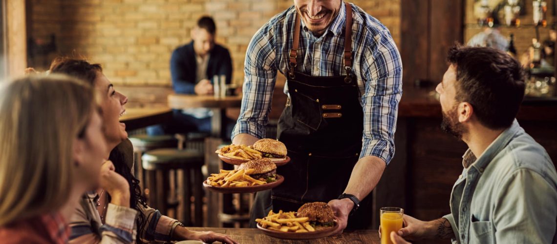 happy-waiter-serving-food-group-cheerful-friends-pub
