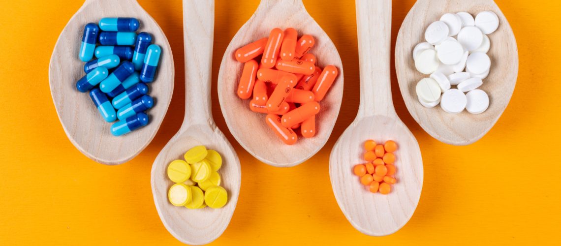 top-view-colorful-pills-wooden-spoons-orange-background-horizontal